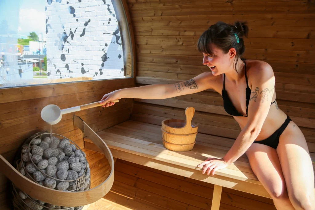 Girl pouring water on HUUM sauna heater in a Thermory Barrel Saunas