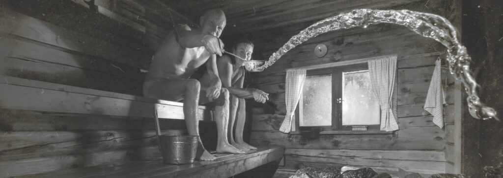 Two people relaxing in a sauna, throwing water on the heater.
